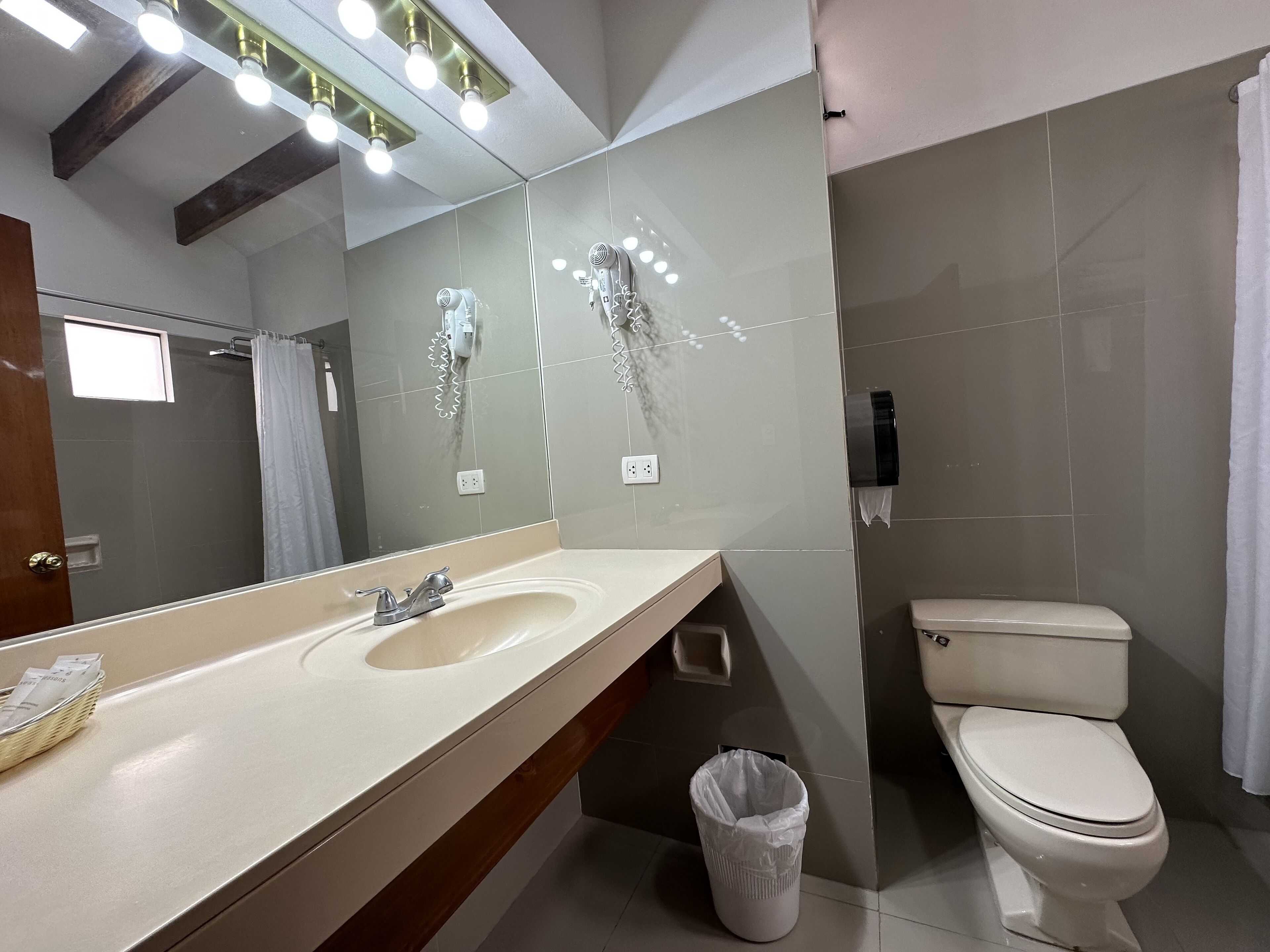 A modern bathroom with a large mirror, a sink, a toilet, and a trash bin.
