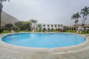 Uma piscina com deck revestido, rodeada por espreguiçadeiras e palmeiras.