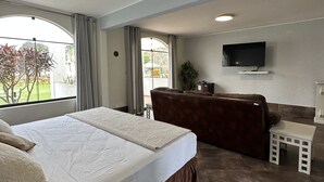 Habitación de hotel con una cama grande, un sofá, un televisor montado en la pared y vistas al exterior.