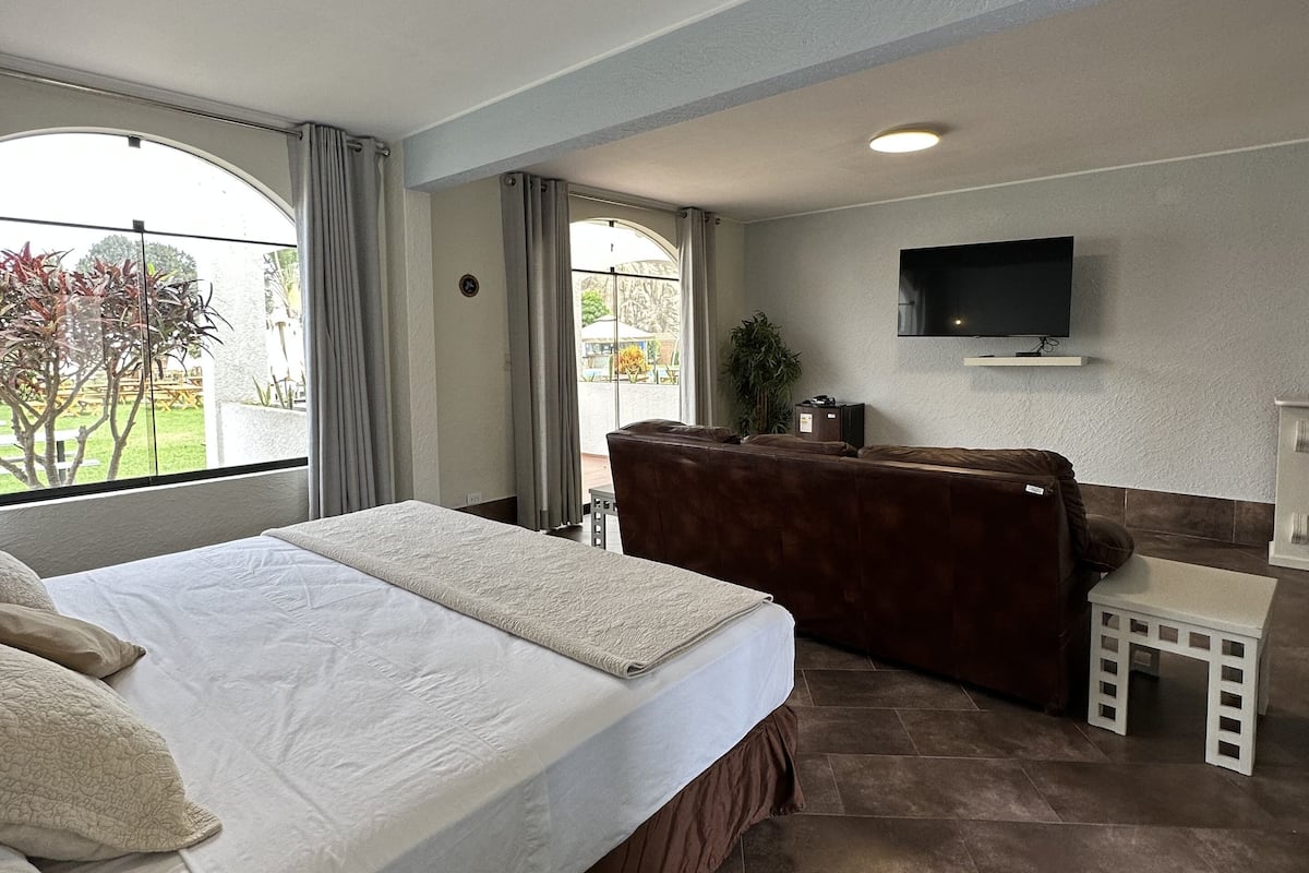 Habitación de hotel con una cama grande, un sofá, un televisor montado en la pared y vistas al exterior.