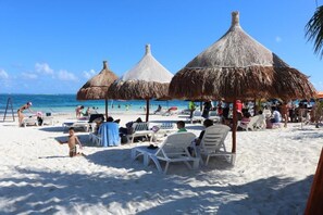 A beach with thatched umbrellas, sun loungers, and people relaxing.