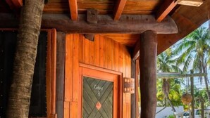 A wooden door with a geometric pattern, a doormat, and a wooden deck leading to a covered area with a view of palm trees. - The Diving Lodge Downtown (Puerto Morelos)