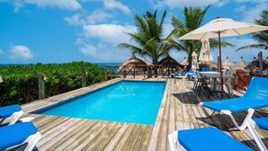 A wooden deck with a pool, blue lounge chairs, and umbrellas. - The Diving Lodge Downtown (Puerto Morelos)