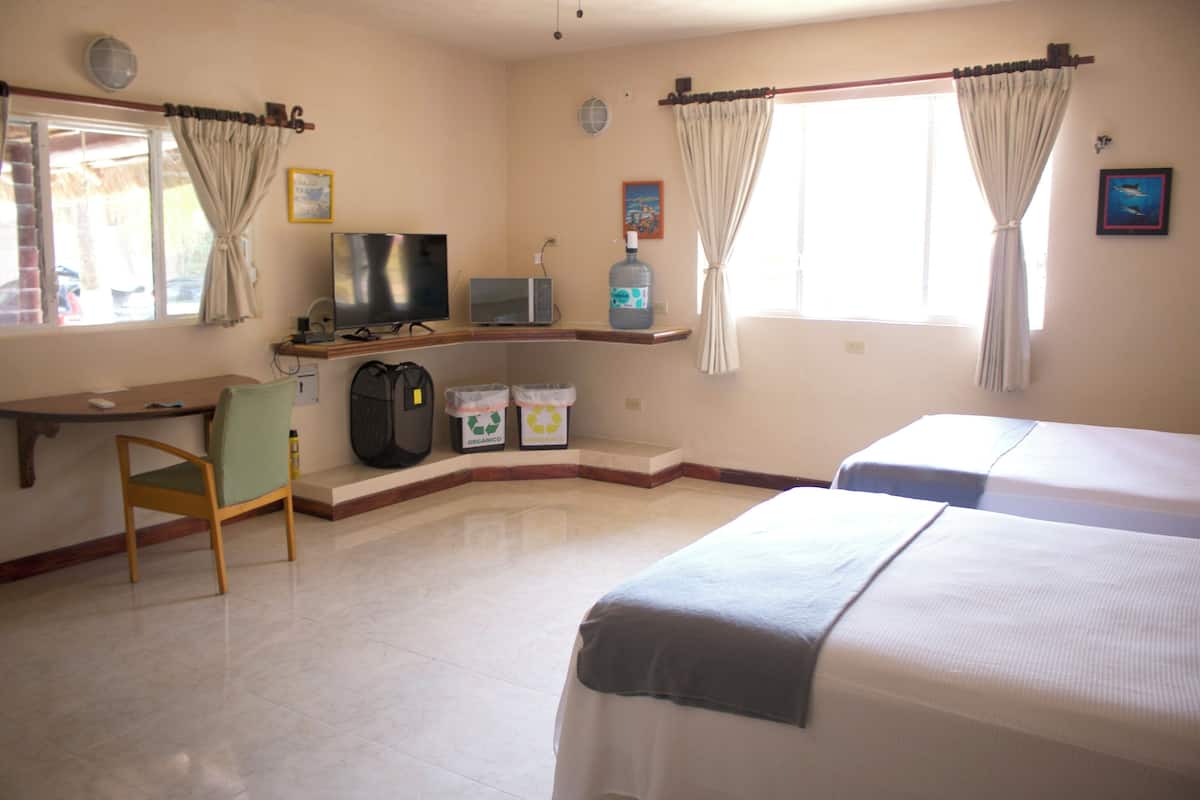 A hotel room with two beds, a desk with a television, a chair, and a window with curtains.
