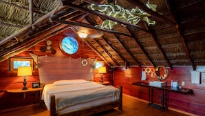 A cozy attic bedroom with a wooden bed, a nightstand, a table with a mirror, and a ceiling fan. - The Diving Lodge Downtown (Puerto Morelos)