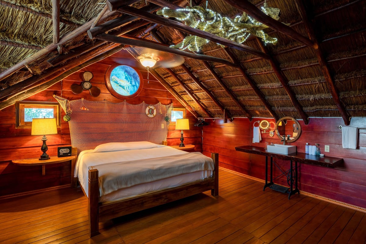 A cozy attic bedroom with a wooden bed, a nightstand, a table with a mirror, and a ceiling fan.