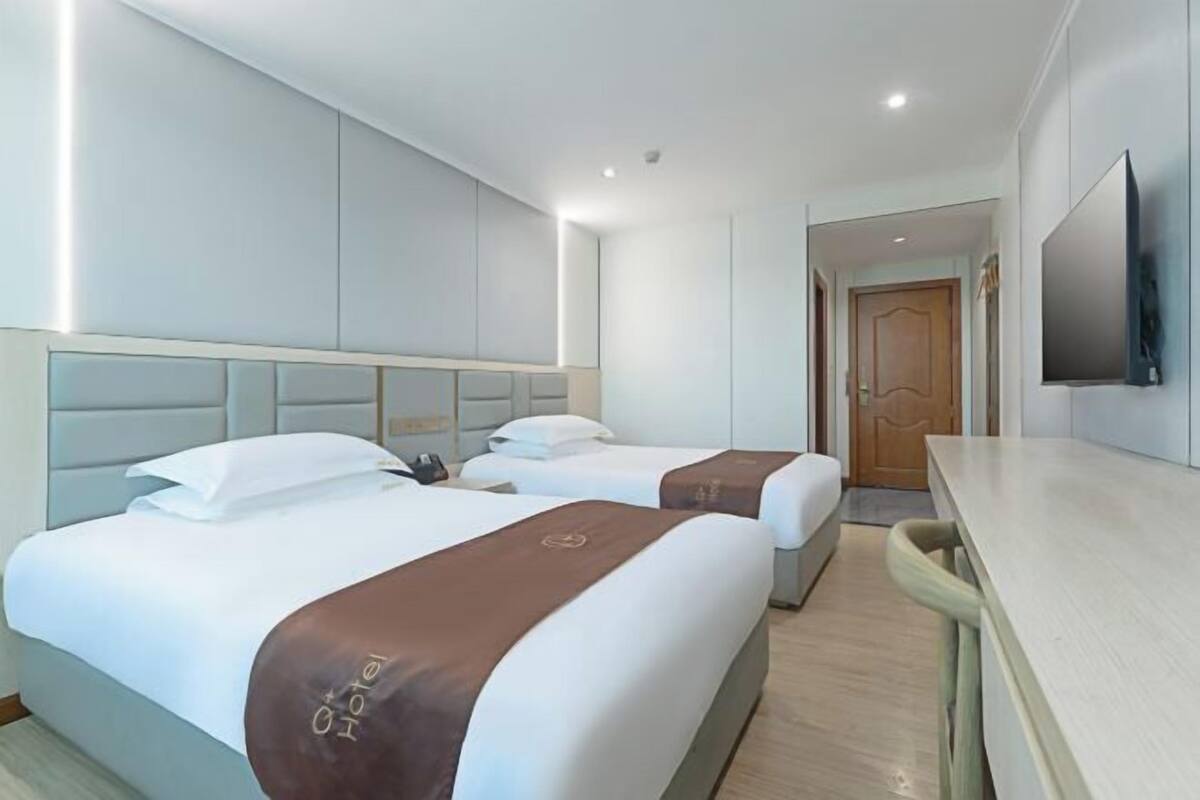 A hotel room with two beds, a desk, and a TV mounted on the wall.