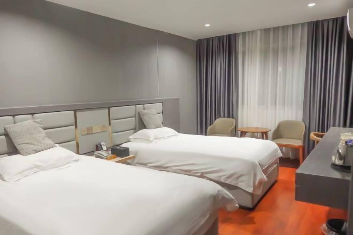 A hotel room with two beds, a desk, a chair, and a small table.