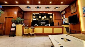 A hotel reception area with a wooden reception desk, two bar stools, a large bed, and a television on the wall. - Q+ Shicheng Zuguoshun Hotel (Shicheng County Bus Station) (Shicheng)