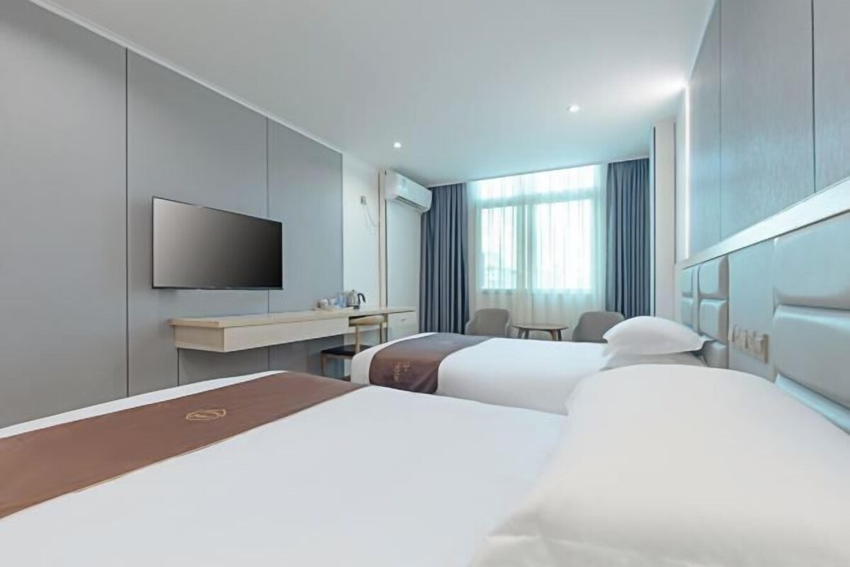 Ett hotellrum med två sängar, en platt-TV, ett skrivbord med en stol och ett fönster med gardiner.