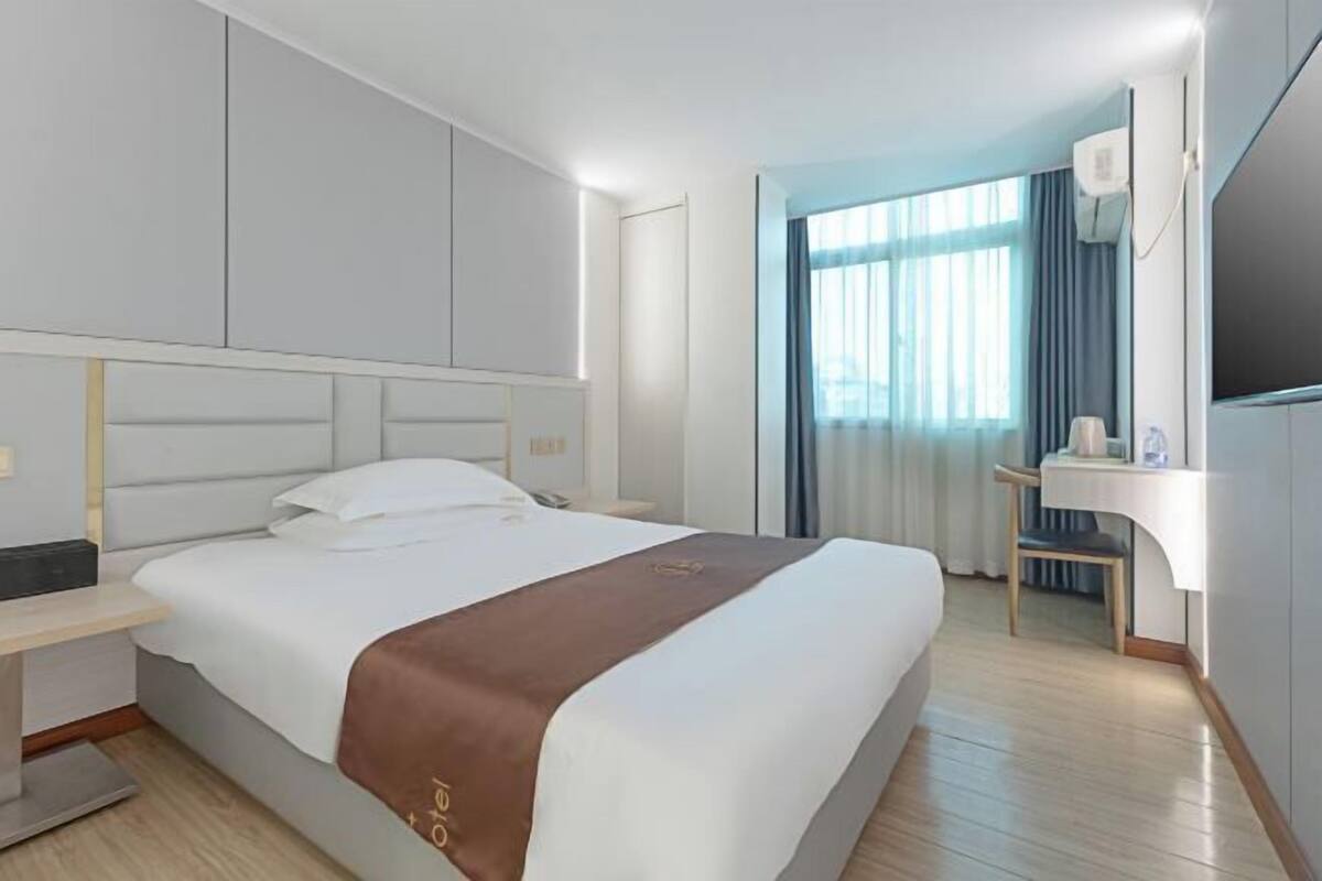 A hotel room with a bed, bedside table, and a mirror.