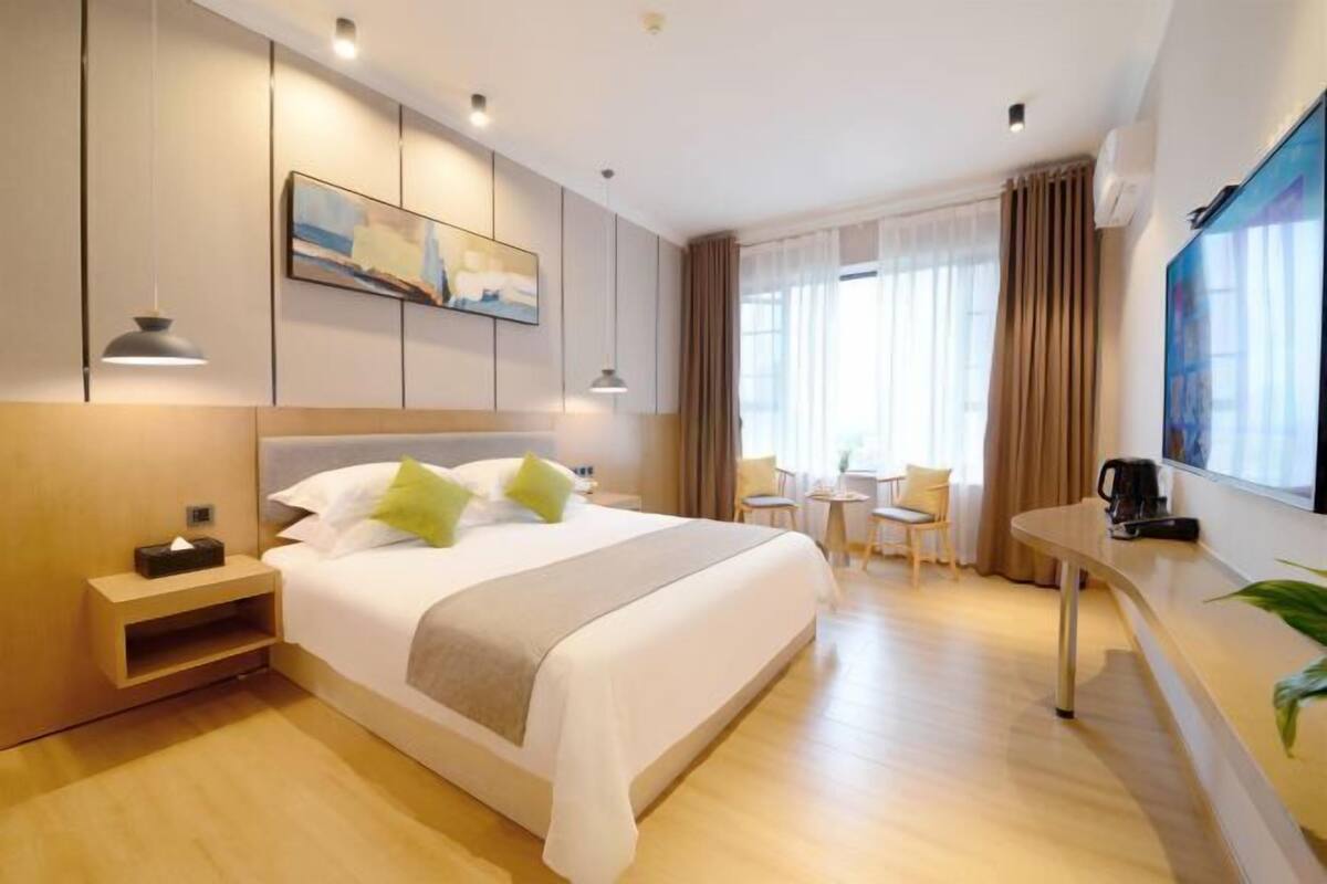 A modern hotel room with a large bed, bedside tables, a desk, and a view of the outdoors.