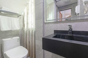 Ett modernt badrum med en vit toalett, en svart handfat och en spegel ovanför handfatet.