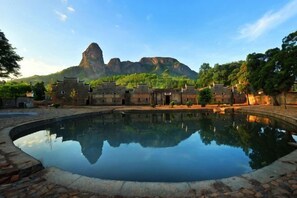 Un patio con un estanque reflectante, edificios tradicionales y una montaña al fondo.