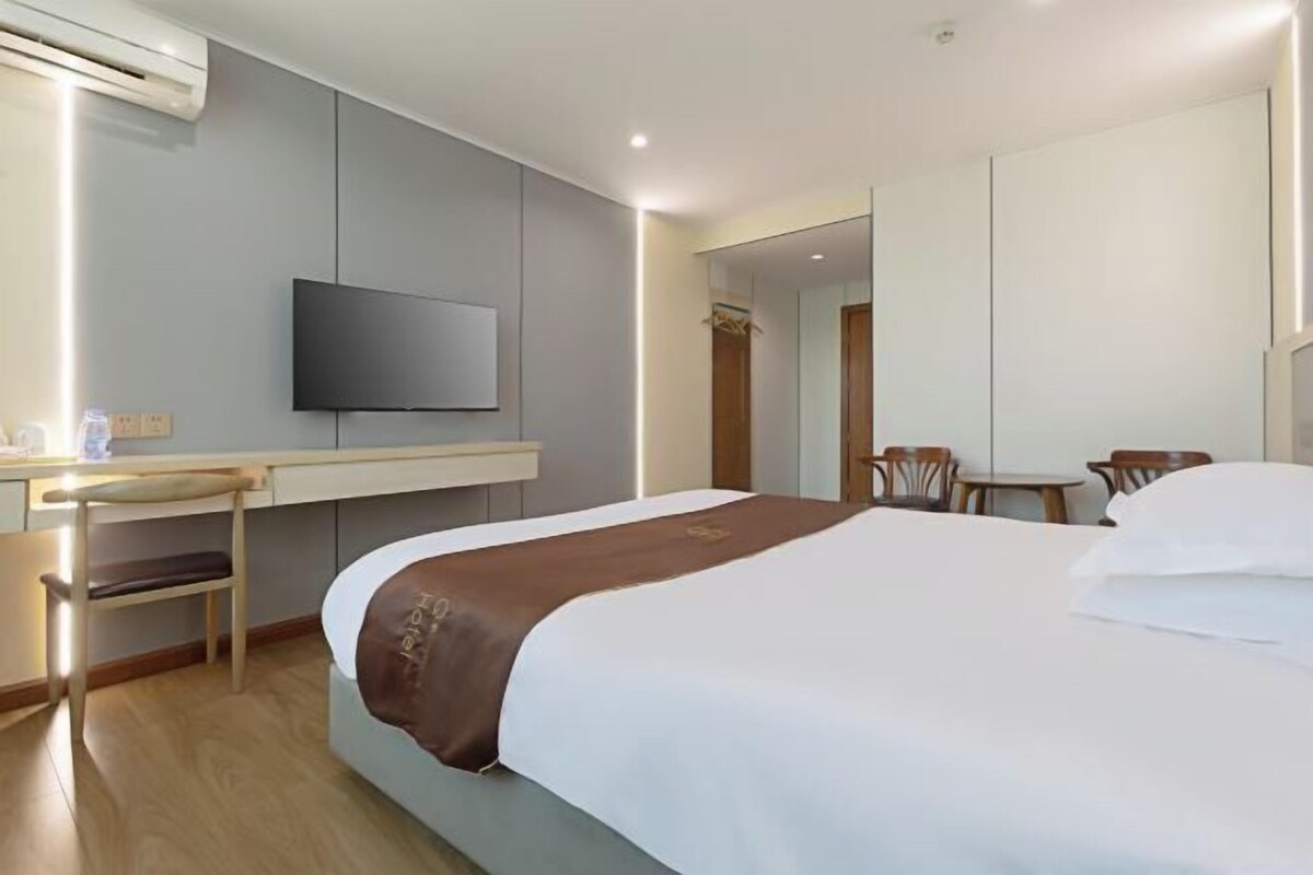 Ett hotellrum med en säng, ett skrivbord, en stol, en tv och en spegel.