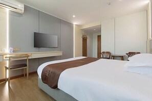 Ett hotellrum med en säng, ett skrivbord, en stol, en tv och en spegel.