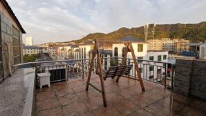 A rooftop terrace with a swing set, stone tiles, and a view of buildings and hills. - Q+ Shicheng Zuguoshun Hotel (Shicheng County Bus Station) (Shicheng)