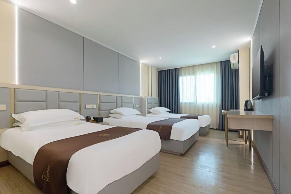 Ett hotellrum med två sängar, ett skrivbord, en platt-TV och ett fönster med gardiner.