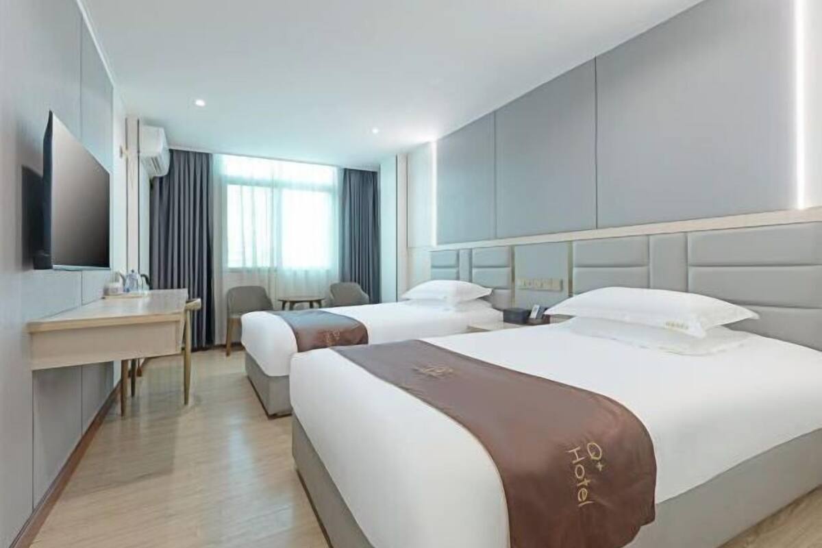 A hotel room with two beds, a desk, a chair, and a TV.