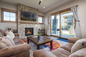 A living room with a stone fireplace, leather couches, a wooden coffee table, and a large sliding glass door to the outside.