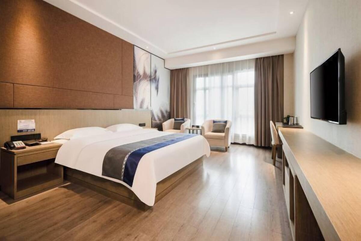 Une chambre d’hôtel avec un grand lit, un bureau, une chaise, une télévision et une fenêtre avec des rideaux.