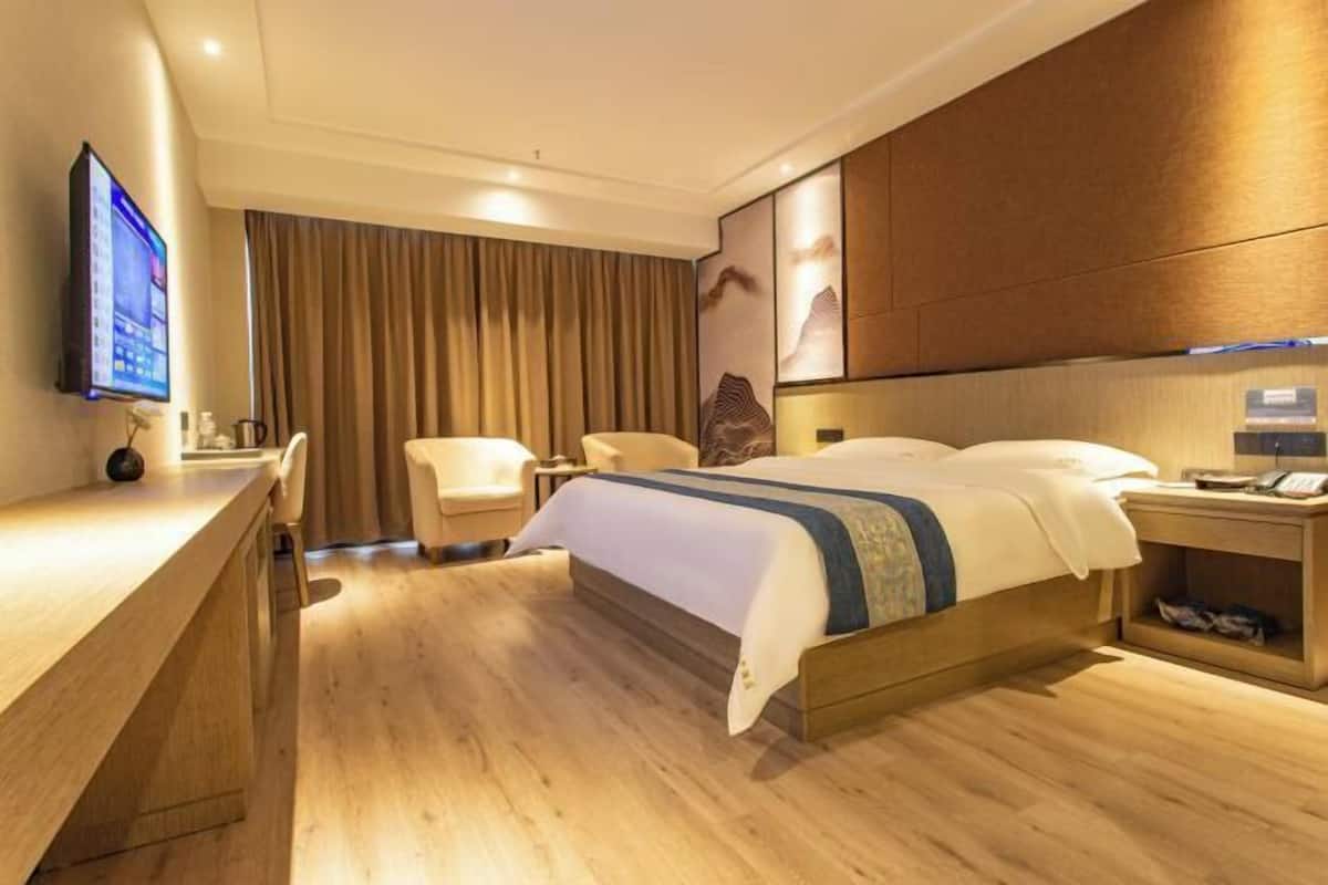 A hotel room with a bed, a desk, a chair, a TV, and a wooden floor.