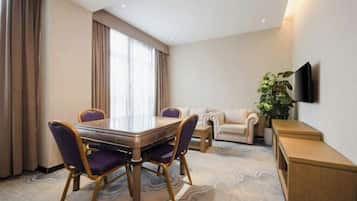 A hotel room with a dining table, two chairs, a sofa, a TV mounted on the wall, and a plant.