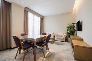 A hotel room with a dining table, two chairs, a sofa, a TV mounted on the wall, and a plant. - Sanfeng Hotel (Nanning)