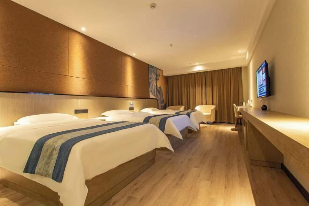 A hotel room with three beds, a wooden floor, a flat-screen TV, and a desk.