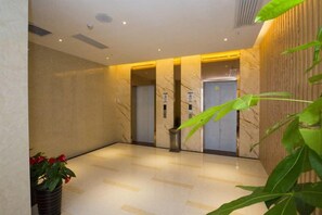 Un hall d’hôtel avec un sol en marbre, des ascenseurs et une plante en pot.