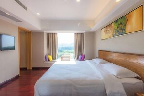 A hotel room with a large bed, a TV on the wall, and a window with curtains.
