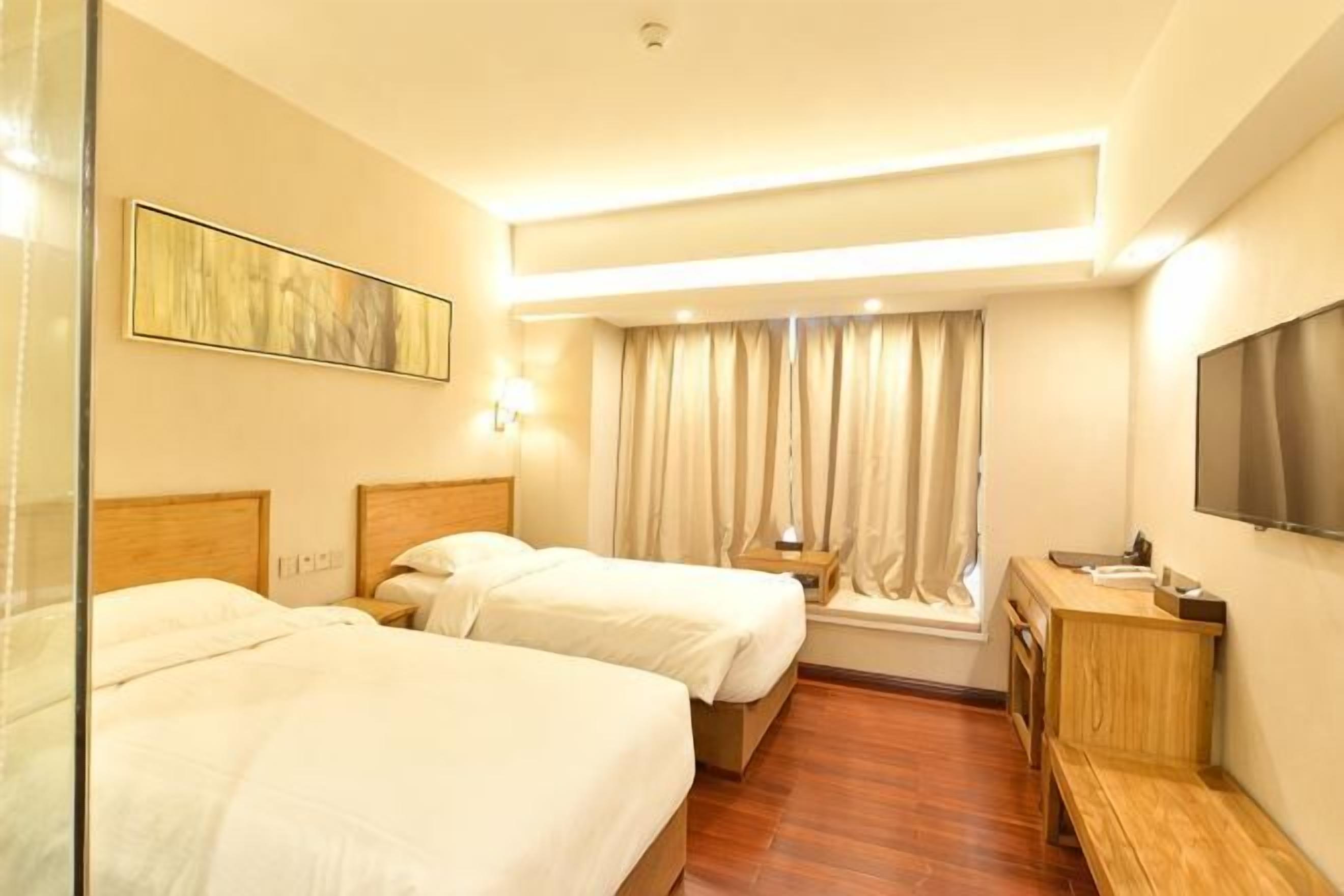 A hotel room with two beds, a TV, a desk, and a window with curtains.