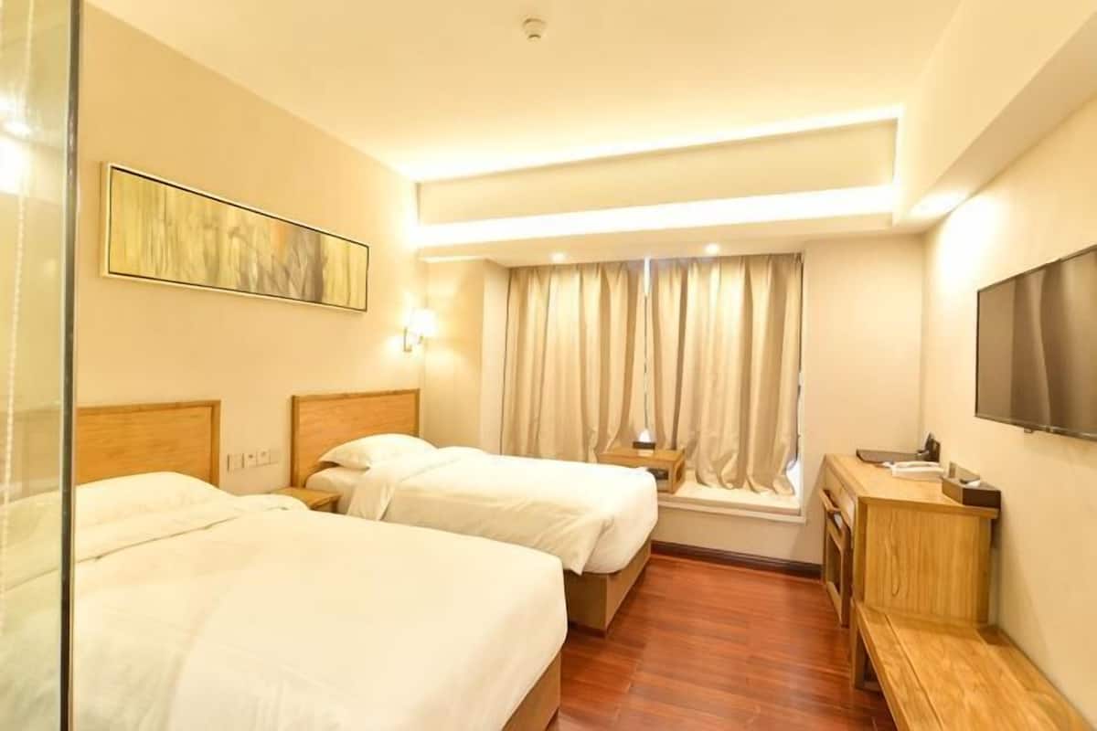 A hotel room with two beds, a TV, a desk, and a window with curtains.