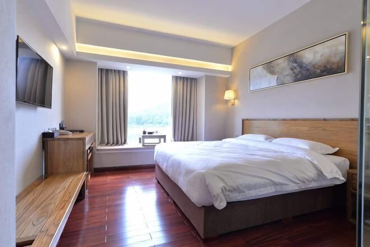 A hotel room with a large bed, a desk, a bench, a TV, and a window with curtains.