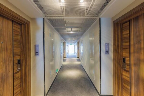 A hotel corridor with wooden doors, a carpeted floor, and a ceiling with recessed lighting. - The Elms lnn(Zhuhai BNBU) (Zhuhai)
