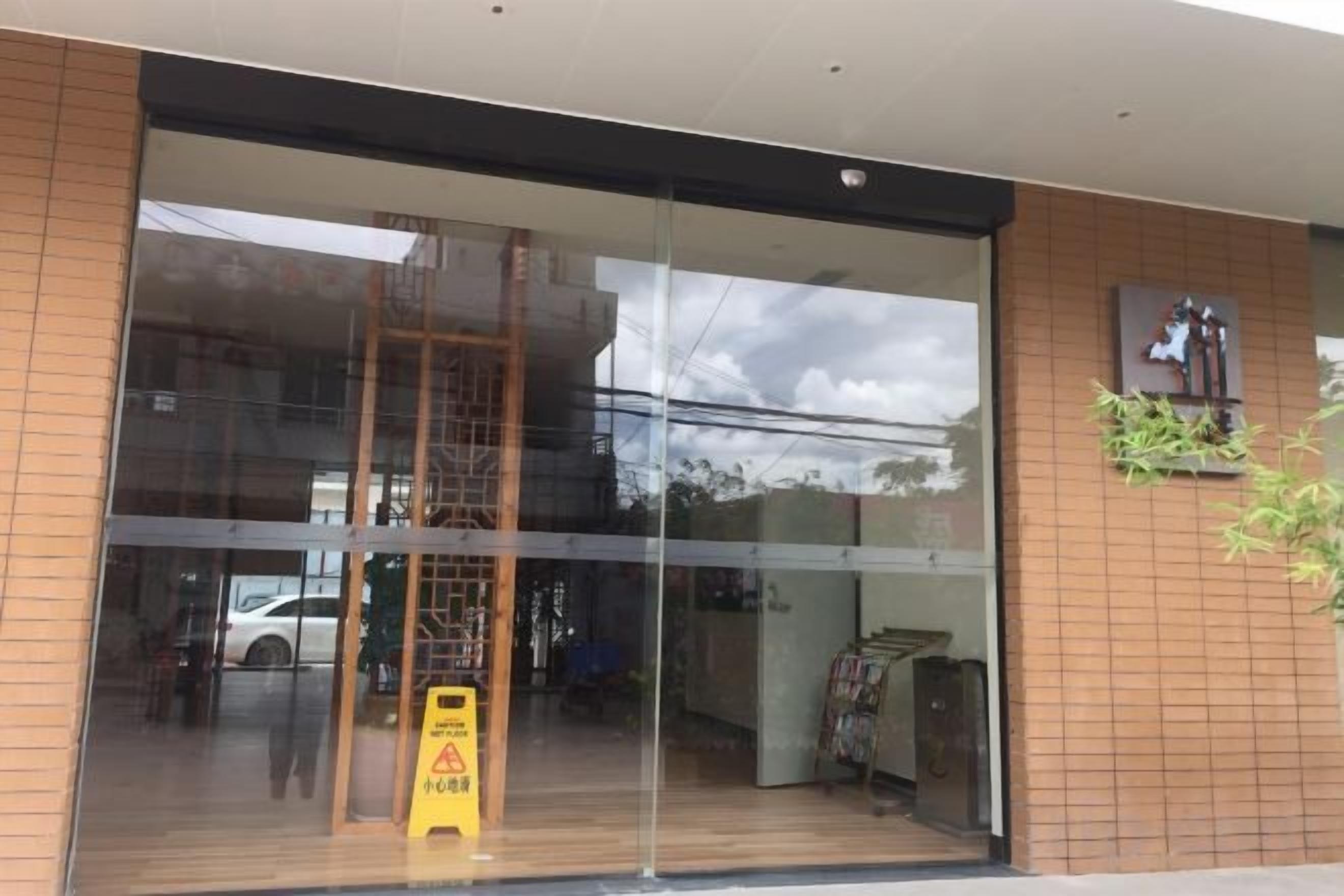 A building entrance with a large glass door, a wooden floor inside, and a caution sign outside.