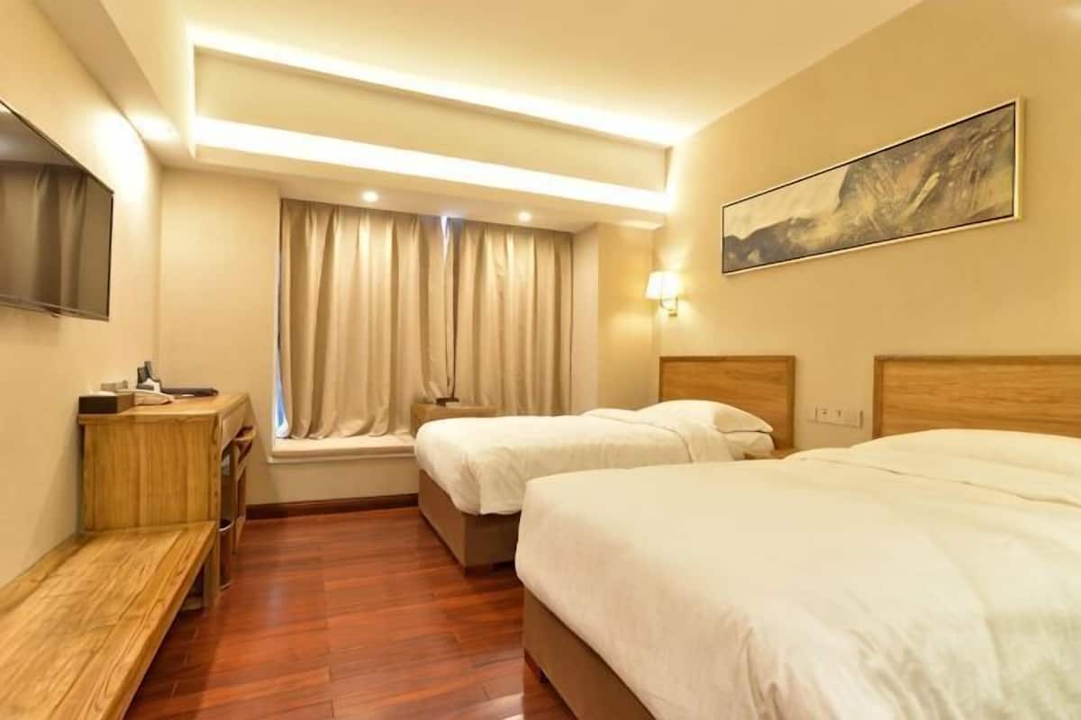A hotel room with two beds, a desk, a TV, and a window with curtains.