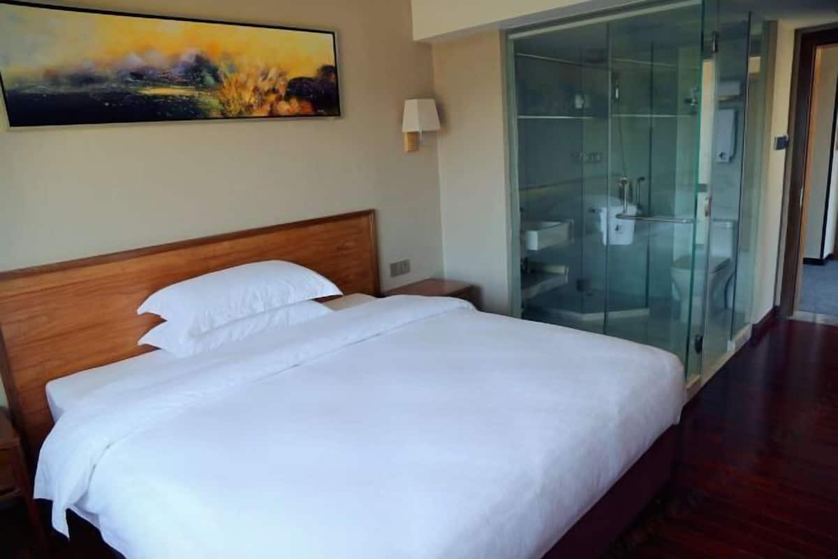 A hotel room with a wooden bed, a glass shower enclosure, and a painting on the wall.