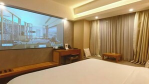Habitación de hotel con una cama grande, un escritorio con una silla, una pantalla de televisión y una cortina.