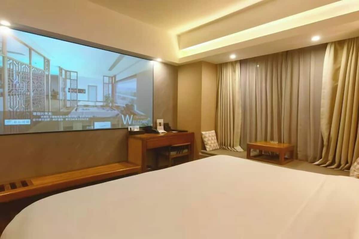 A hotel room with a large bed, a desk with a chair, a TV screen, and a curtain.