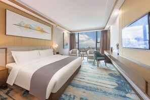 A hotel room with a large bed, a desk, a chair, and a view of the city.