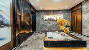 A modern lobby with a marble floor, a vertical wooden panel, a framed artwork, and a yellow floral arrangement. - Chongqing Tongcheng Zhiguang Hotel (Tongnan Branch) (Chongqing)