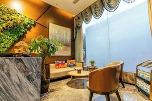 A modern lounge area with a marble reception desk, a sofa with colorful cushions, a round coffee table, and a large window with curtains. - Chongqing Tongcheng Zhiguang Hotel (Tongnan Branch) (Chongqing)