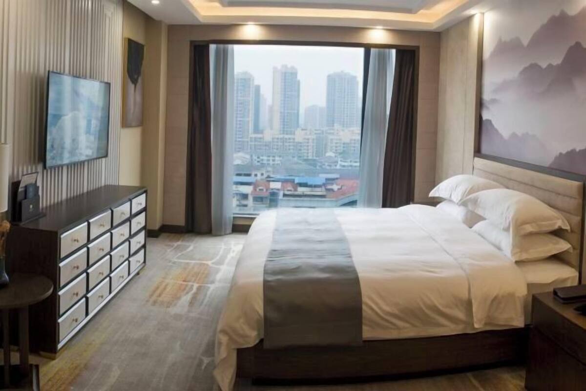 A hotel room with a bed, a desk, a TV, and a city view.