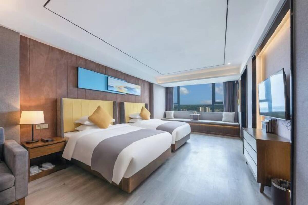 A hotel room with two beds, a TV, a desk, and a view of the city.