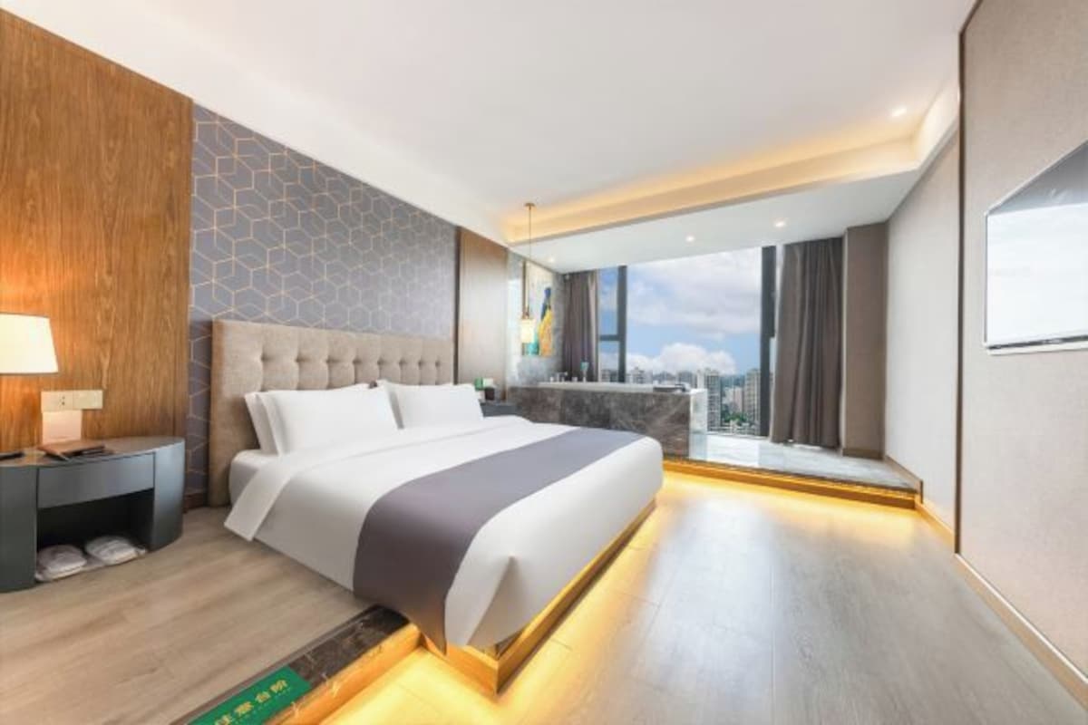 A modern hotel room with a large bed, a nightstand, a view of the city, and a balcony.
