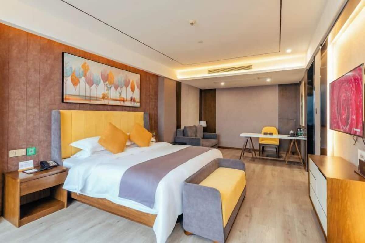 A hotel room with a bed, bedside table, desk, chair, and artwork on the wall.
