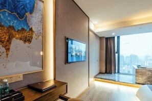 Moderni hotellihuone, jossa on suuri ikkuna, taulutelevisio, työpöytä kannettavalla tietokoneella ja näkymä kaupunkiin.