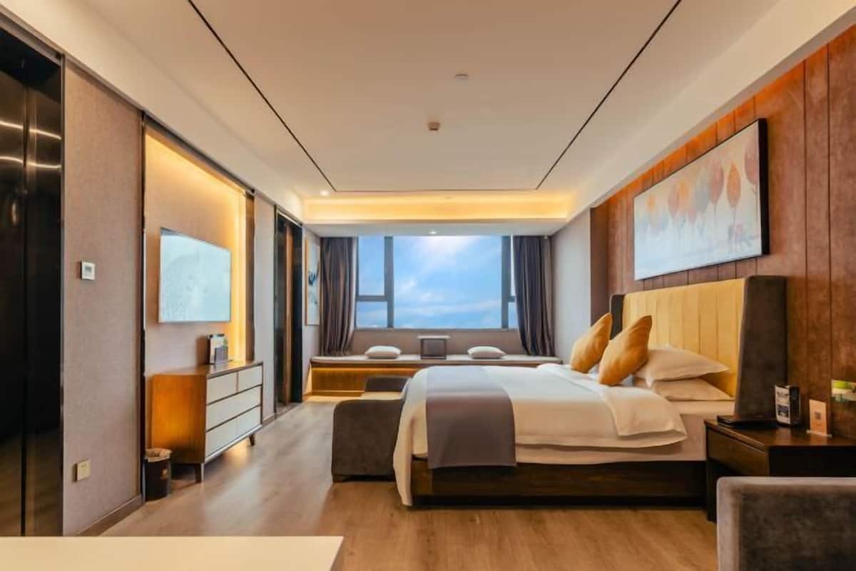 A modern hotel room with a large bed, a desk, a chair, a TV, and a window with curtains.