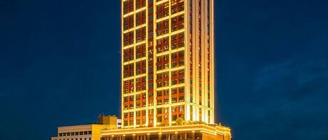 Un hotel de gran altura con varios pisos, ventanas iluminadas y una entrada destacada en la base.